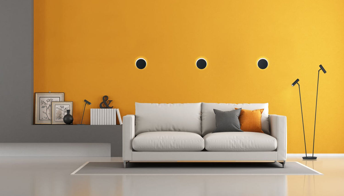 Mise en ambiance de trois appliques murales noires alignées sur un mur jaune