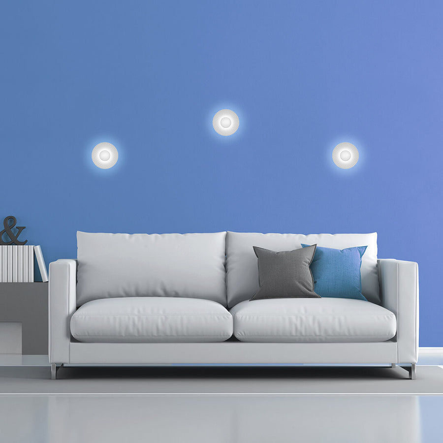 Trois appliques murales allumées sur un mur bleu au-dessus d'un canapé blanc