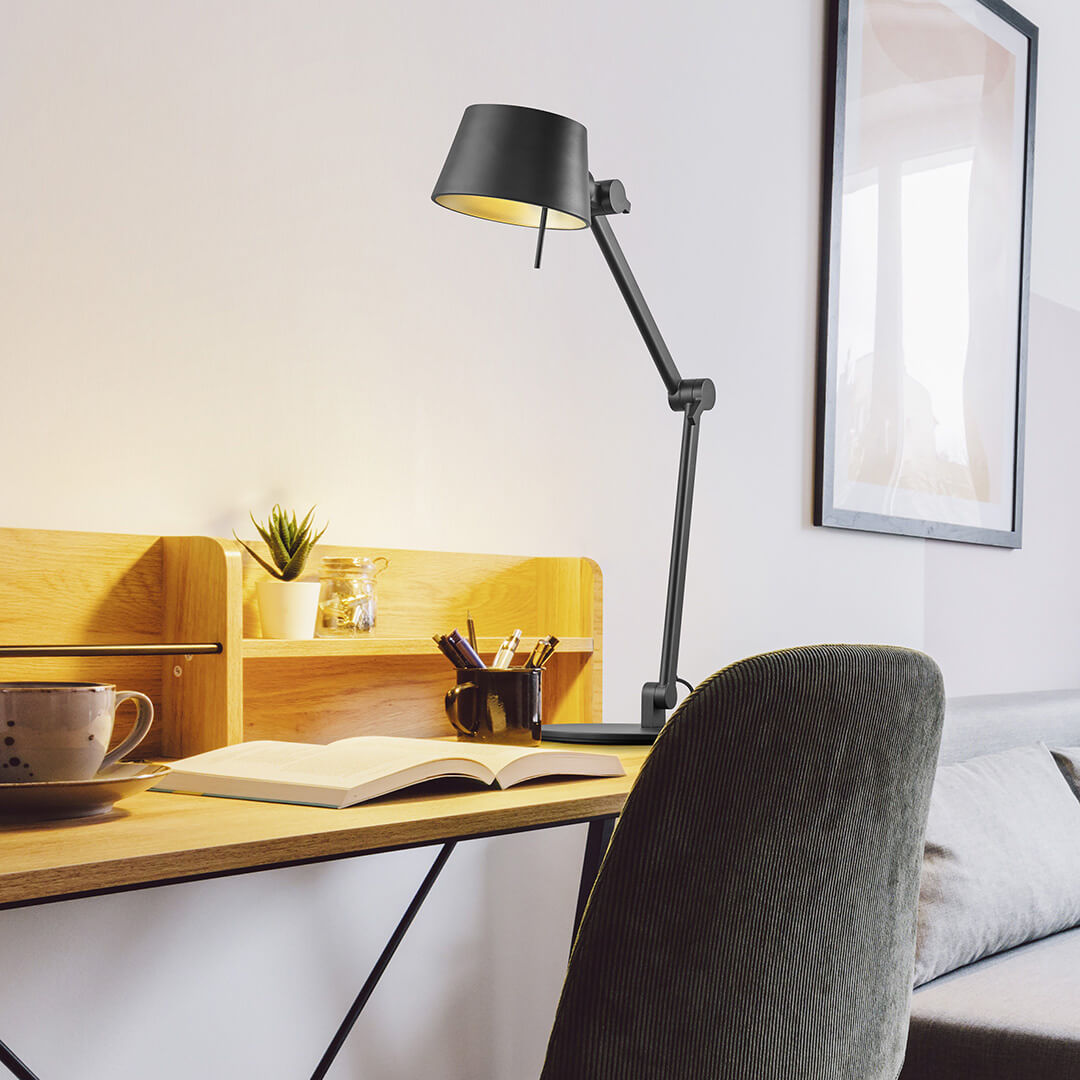 Mise en ambiance sur un bureau en bois, lampe allumée près d'un livre ouvert