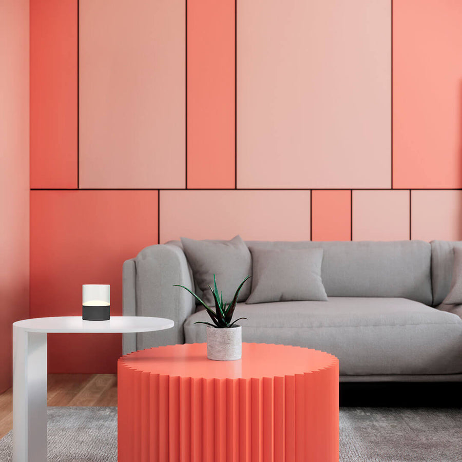 Lampe sans fil posée sur une table basse blanche dans un salon au mur rose géométrique.