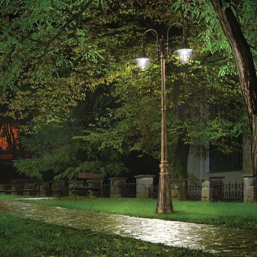 Lampadaire allumé dans un jardin la nuit, éclairant une allée et un banc.