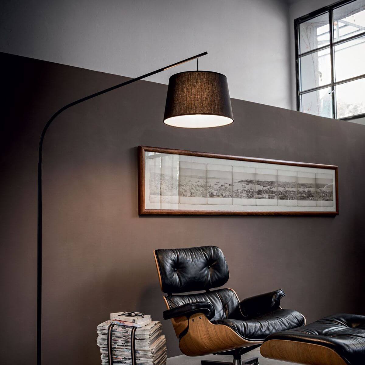 Mise en ambiance salon avec fauteuil cuir noir, tableau panoramique et lampadaire allumé