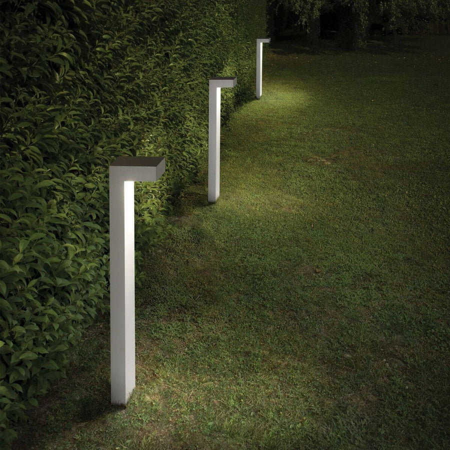 Trois lampadaires extérieurs blancs alignés dans un jardin, éclairage de nuit.