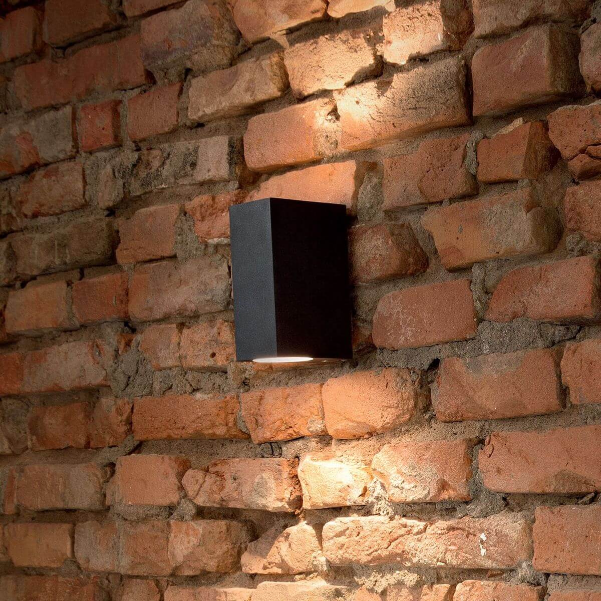 Applique noire allumée sur mur de briques rouges, halo lumineux chaud