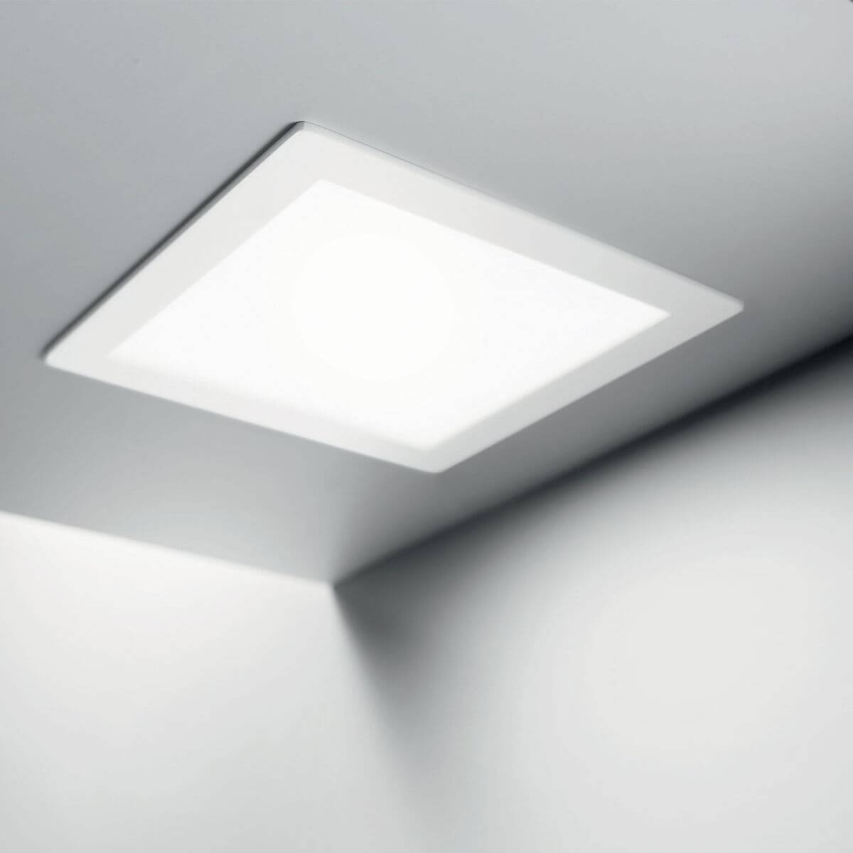Spot carré encastré au plafond blanc, installé et éclairant une pièce.