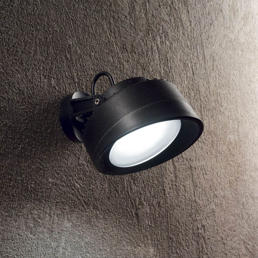 Luminaire mural noir allumé, fixé sur un mur texturé en extérieur