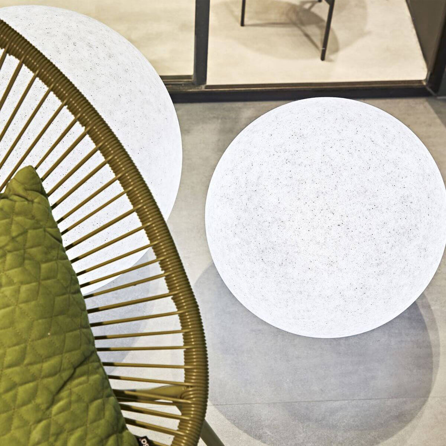 Deux globes lumineux blancs près d'un fauteuil en rotin et coussins verts