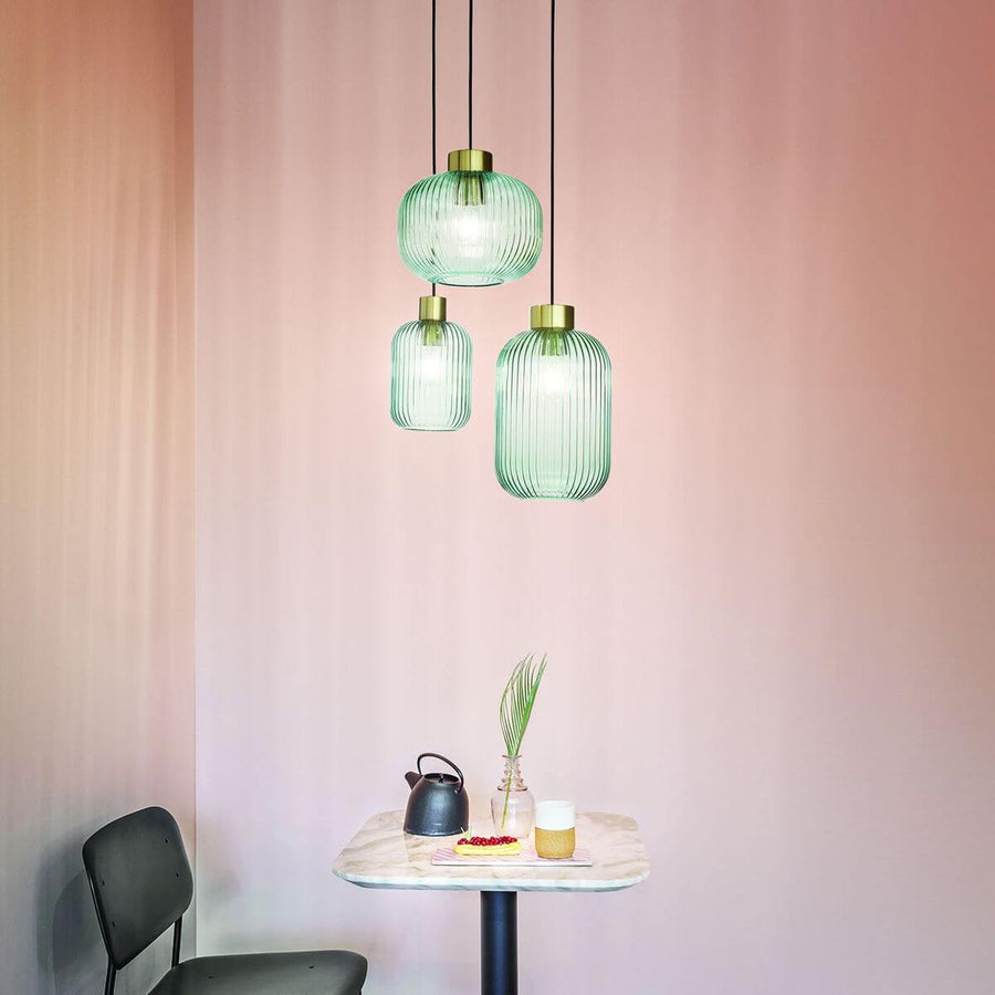 Trois suspensions vertes suspendues au-dessus d'une table dans un décor rose.