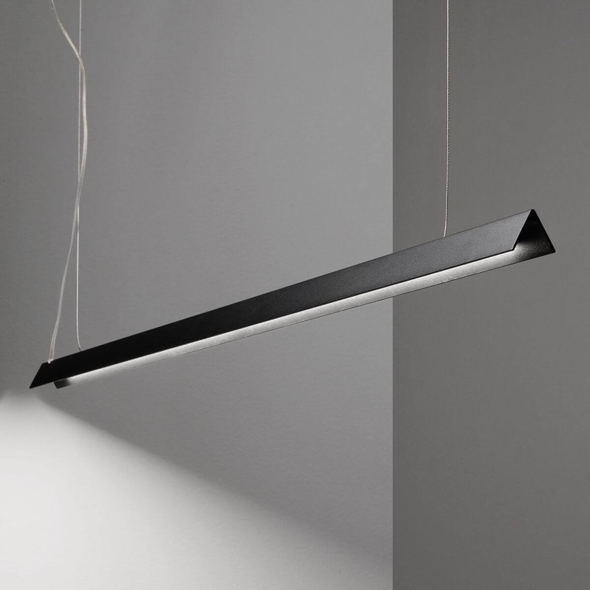 Mise en ambiance du luminaire suspendu au-dessus d'un mur gris, éclairant la pièce.