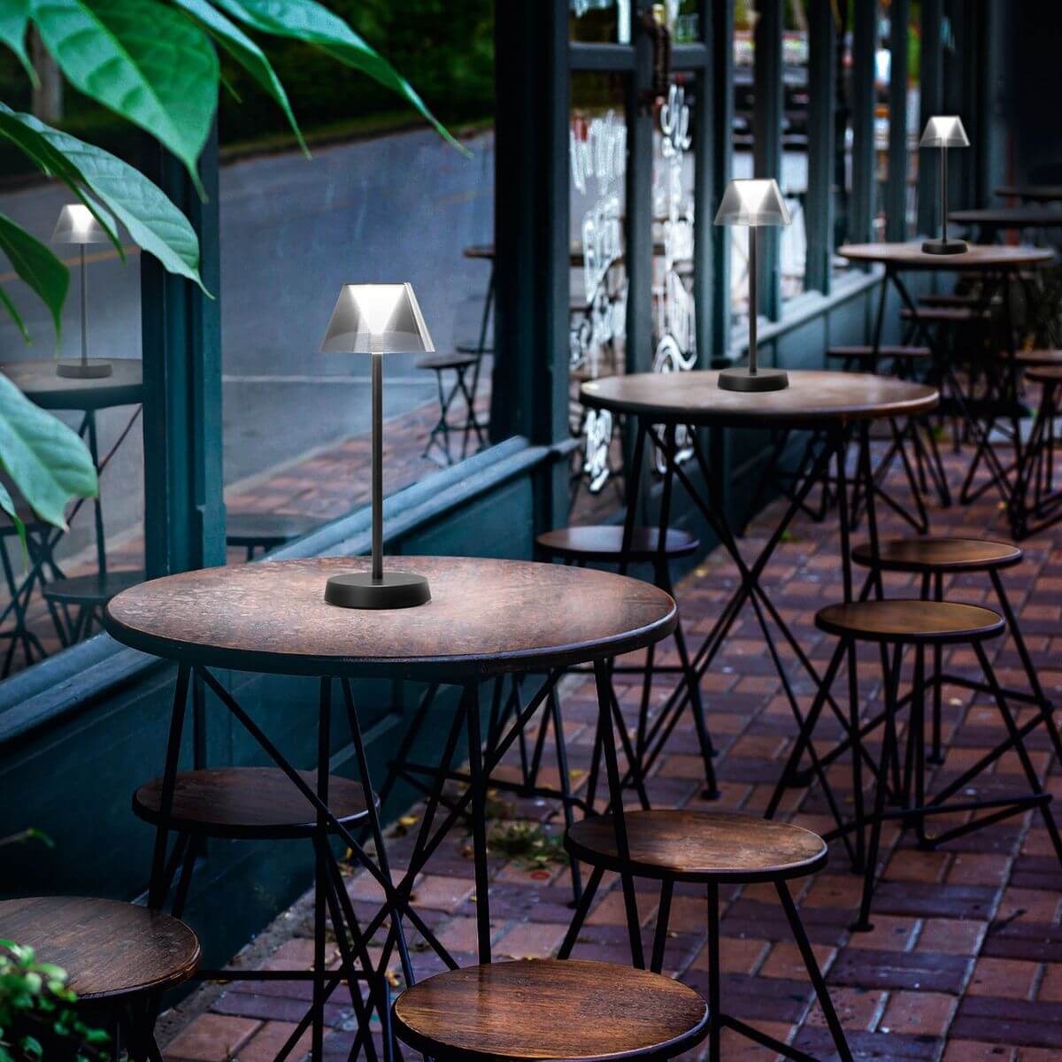 Plusieurs lampes identiques posées sur les tables d'une terrasse de café en extérieur