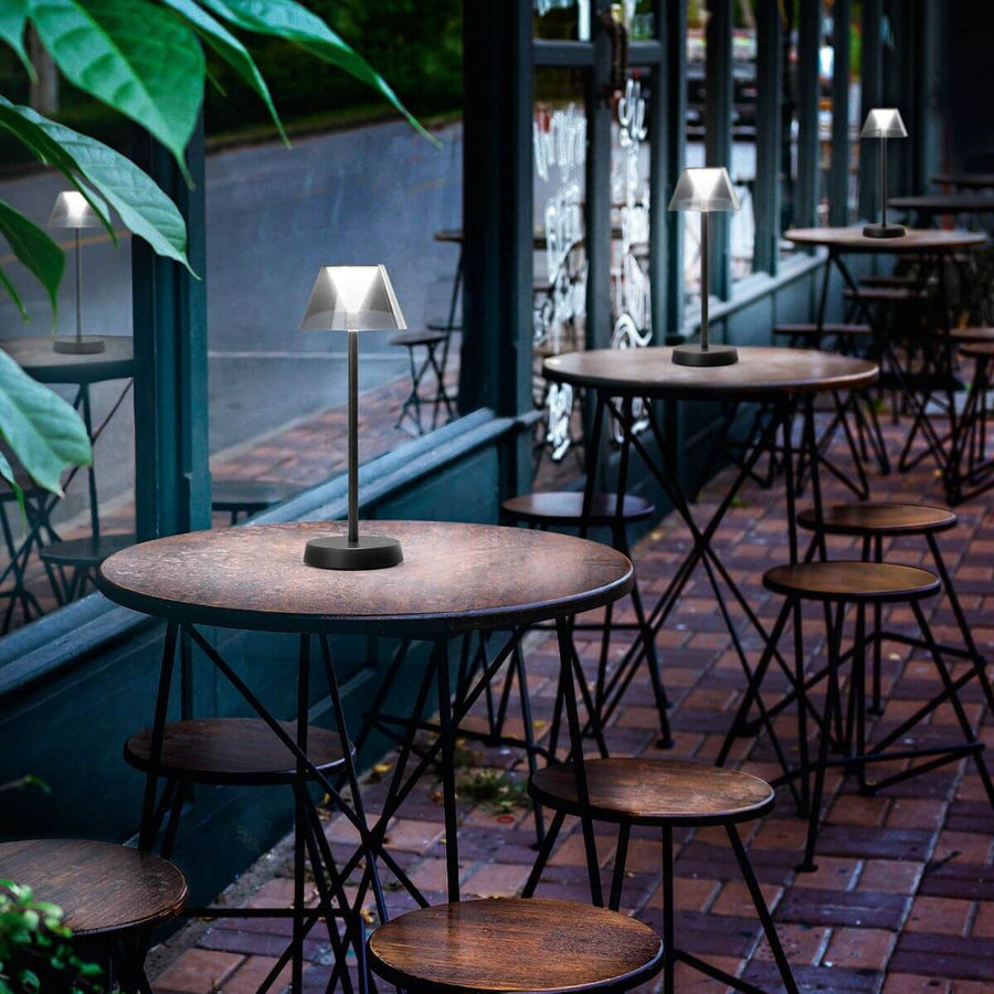 Plusieurs lampes identiques posées sur les tables d'une terrasse de café en extérieur