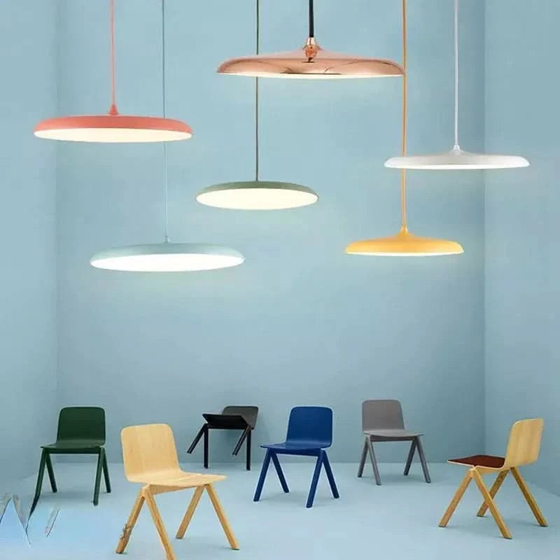 Plusieurs suspensions disque plat colorées allumées sur mur bleu avec chaises design