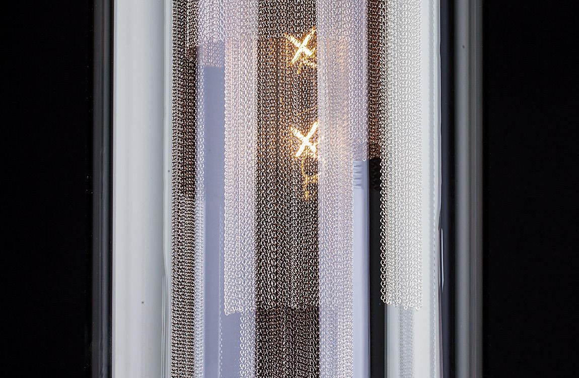 Gros plan sur les chaînettes métalliques et la lumière dorée à l'intérieur du cylindre de verre