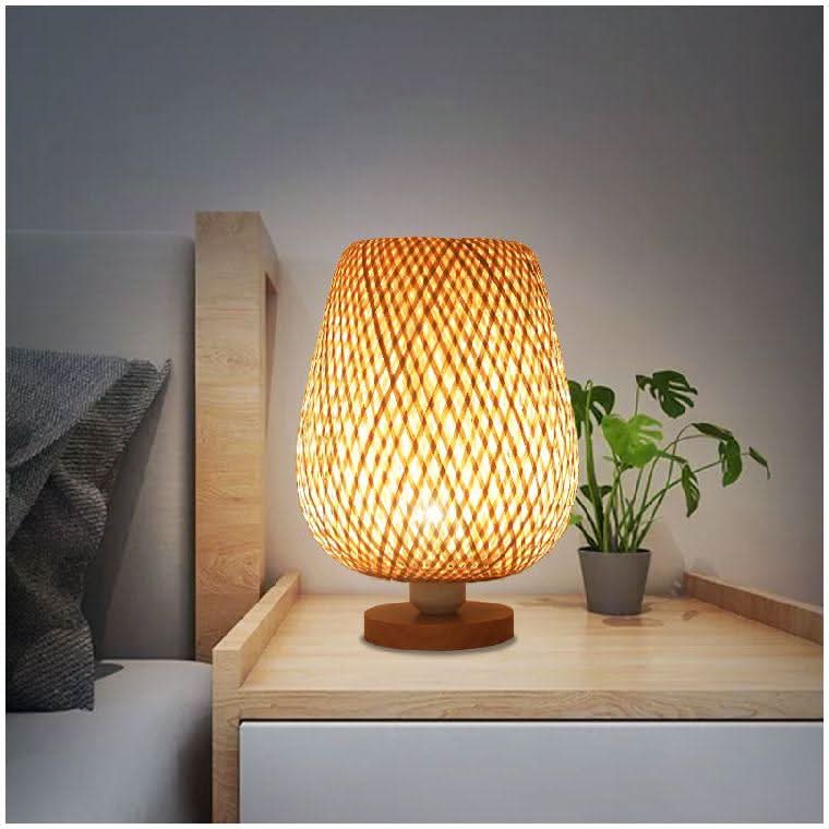 Lampe posée sur une table de chevet en bois clair, petit monstera en pot à côté
