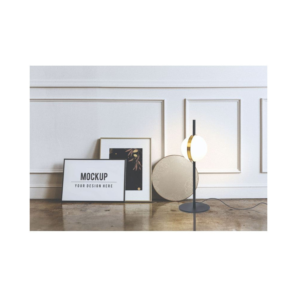 Mise en ambiance: lampe posée au sol près de cadres et plateau rond, mur mouluré.