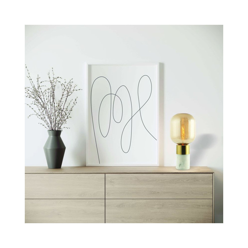 Mise en ambiance sur commode en bois clair, lampe allumée près d'un vase et d'une affiche