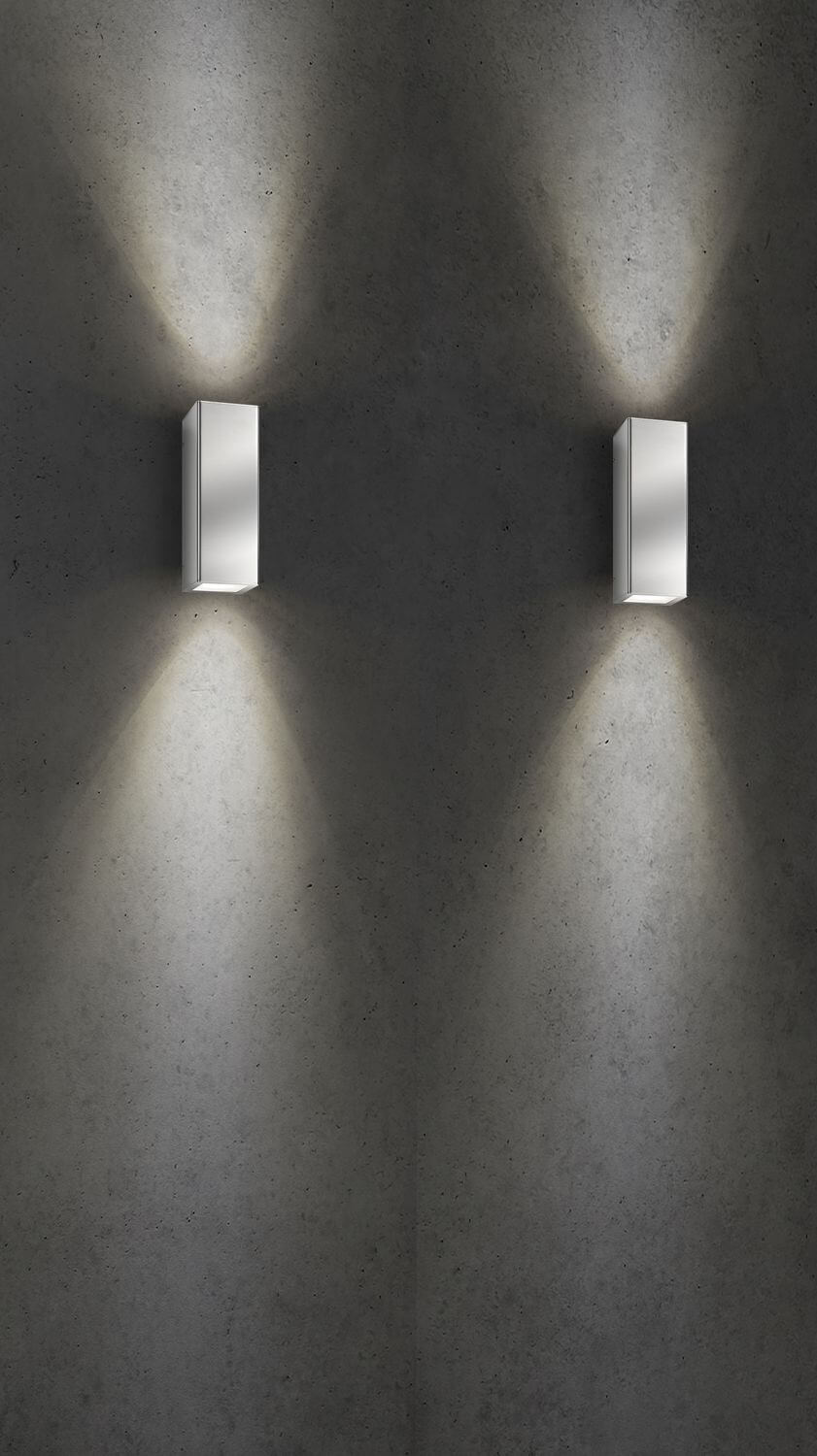 Deux appliques inox fixées sur béton brut, faisceaux lumineux dirigés vers le haut et le bas.