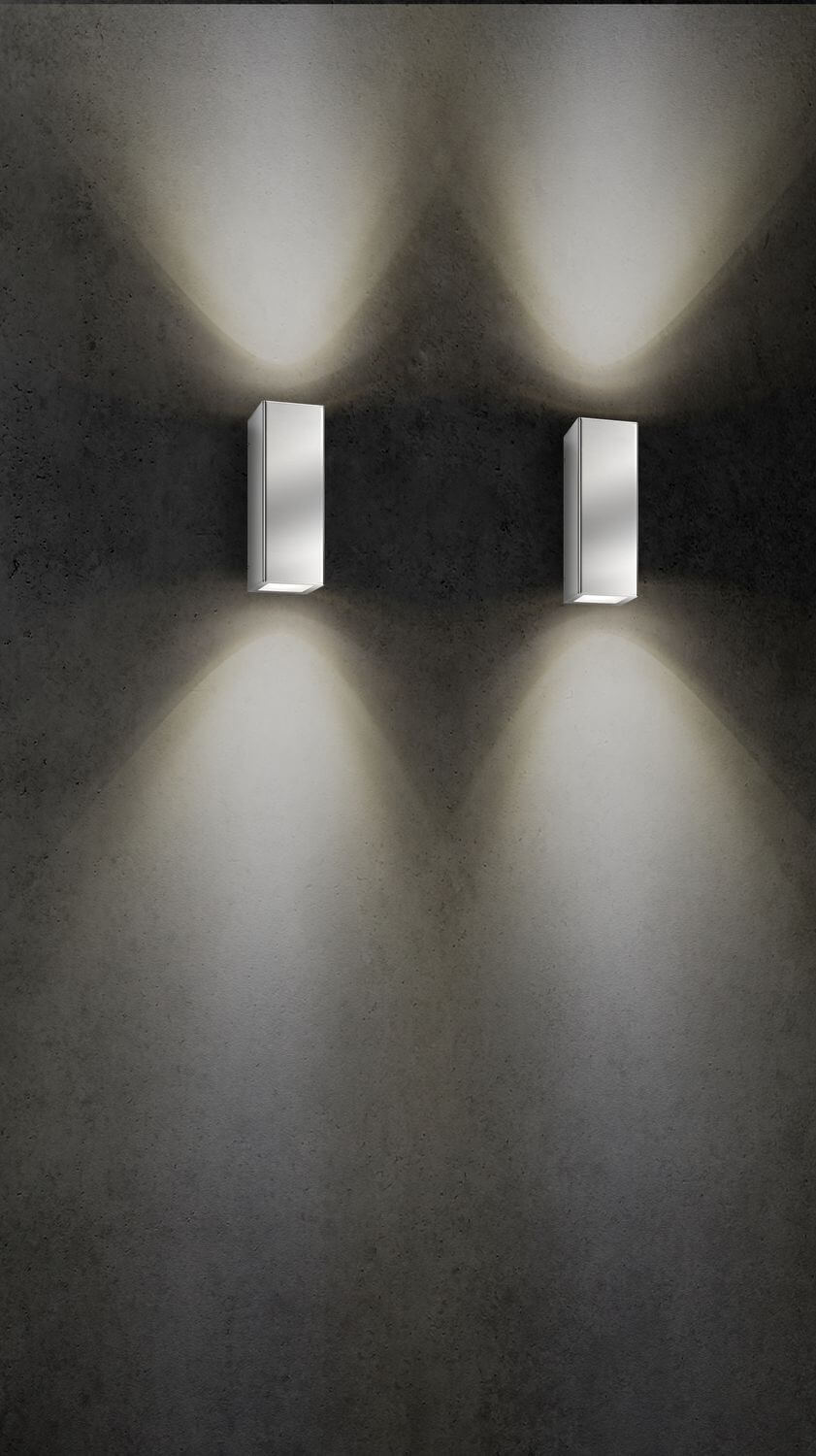 Plan rapproché de deux appliques murales éclairant un mur de béton, lumière blanc chaud.