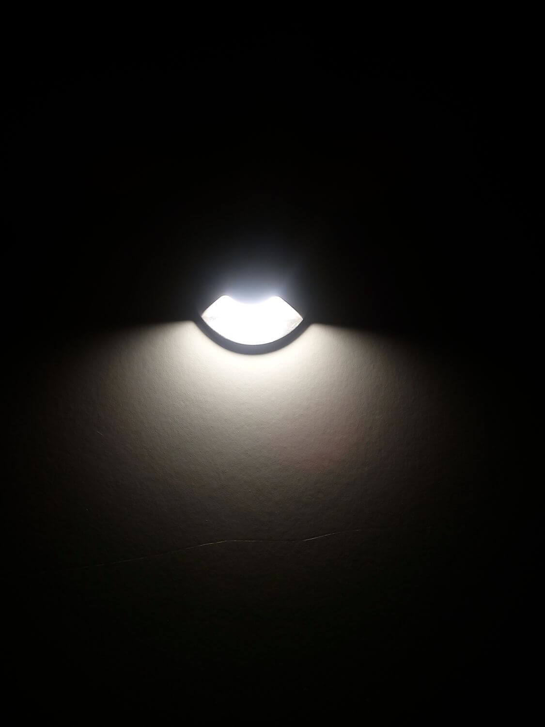 Photo d'ambiance nocturne montrant un luminaire encastré projetant une lumière vive sur un mur.