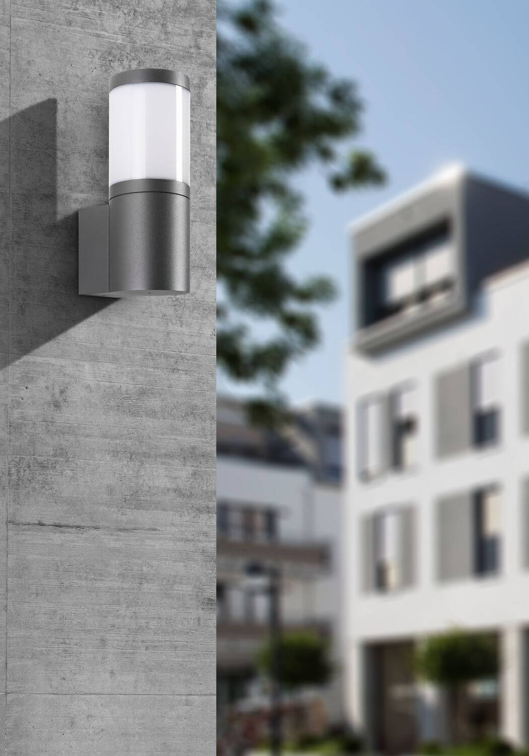 Gros plan de l'applique murale anthracite sur mur béton, arrière-plan urbain flou.