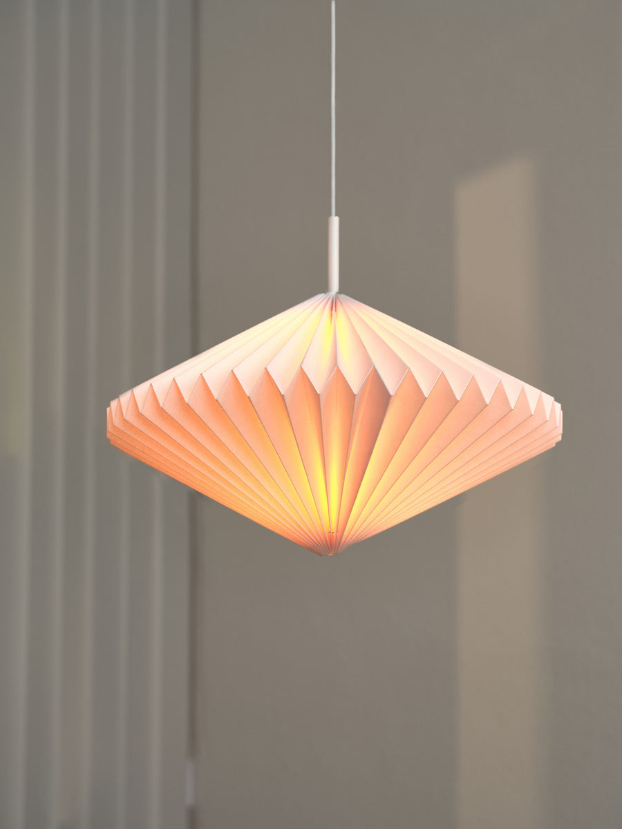 Détail du luminaire allumé, facettes plissées diffusant une lueur orangée douce