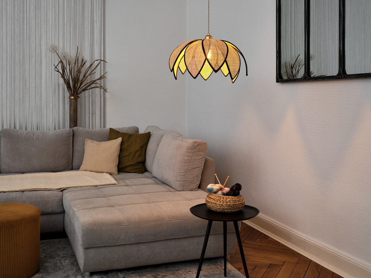 Mise en ambiance salon avec suspension allumée au-dessus d’un canapé gris et table noire.