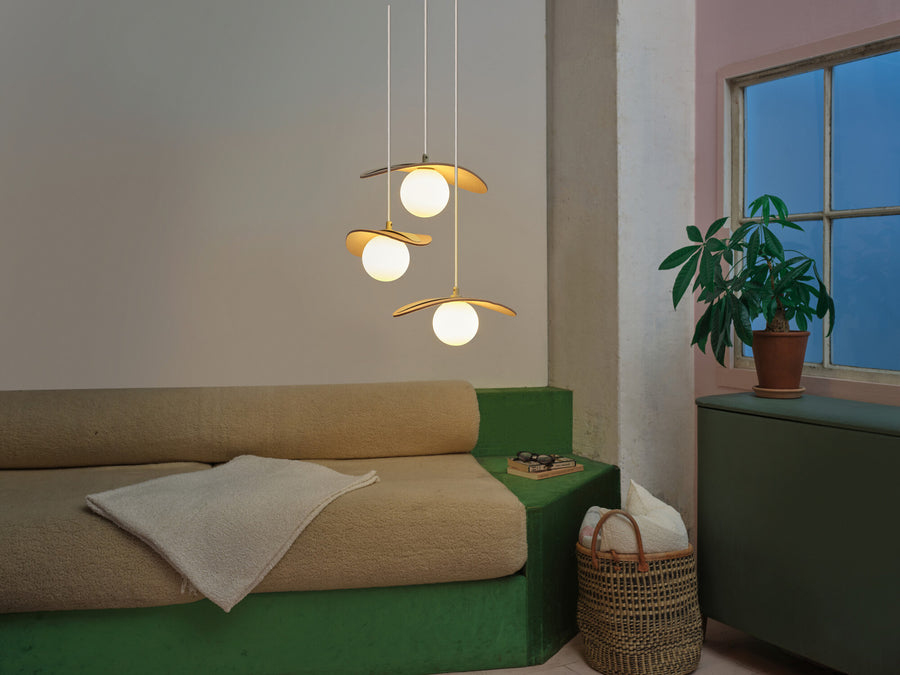 Suspension allumée dans un salon au-dessus d'un canapé vert et beige.