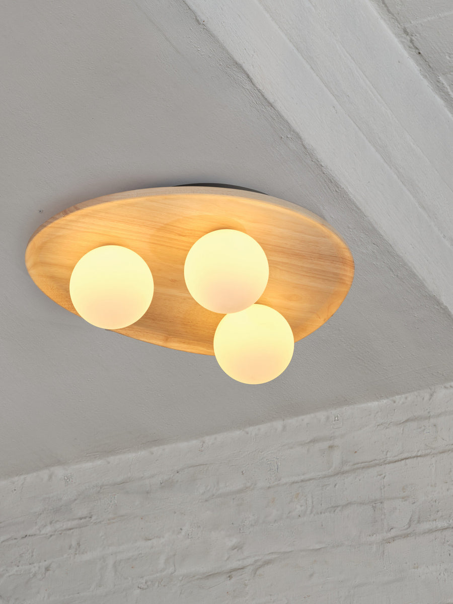 Plafonnier allumé au plafond, plateau ovale en bois et trois globes lumineux.