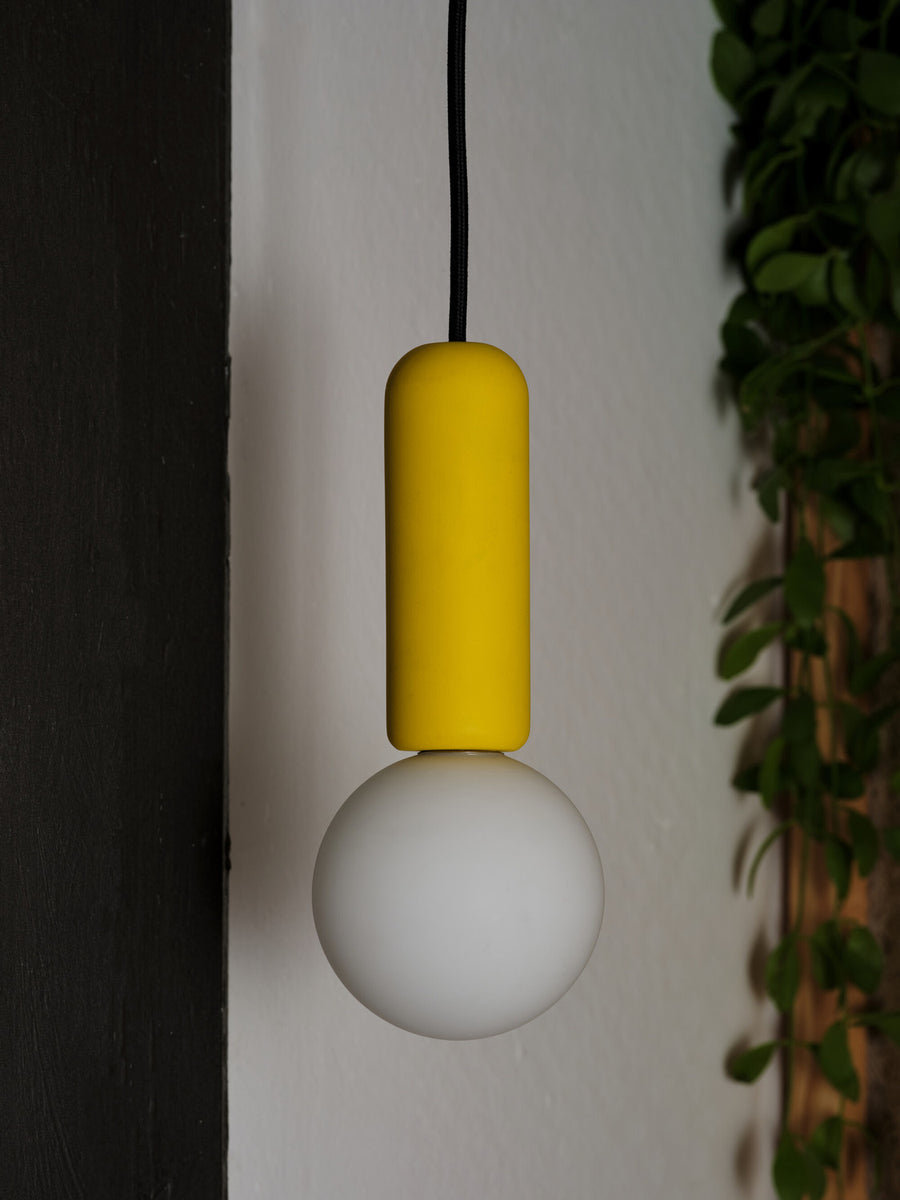 Gros plan du cylindre jaune et du globe blanc allumé, contre un mur.