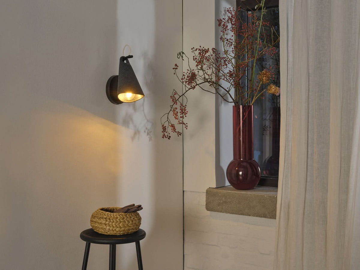 Ambiance chaleureuse avec l'applique murale allumée près d'une fenêtre et d'un vase.