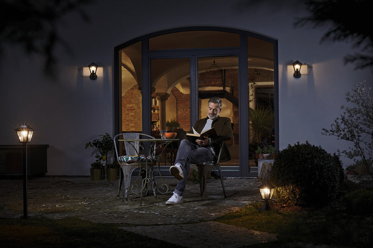 Mise en ambiance nocturne : appliques murales éclairant une terrasse où un homme lit.