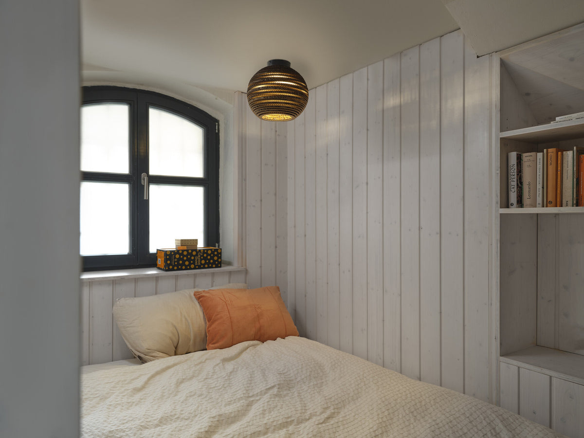 Plafonnier en carton allumé au plafond d'une chambre claire avec lit.