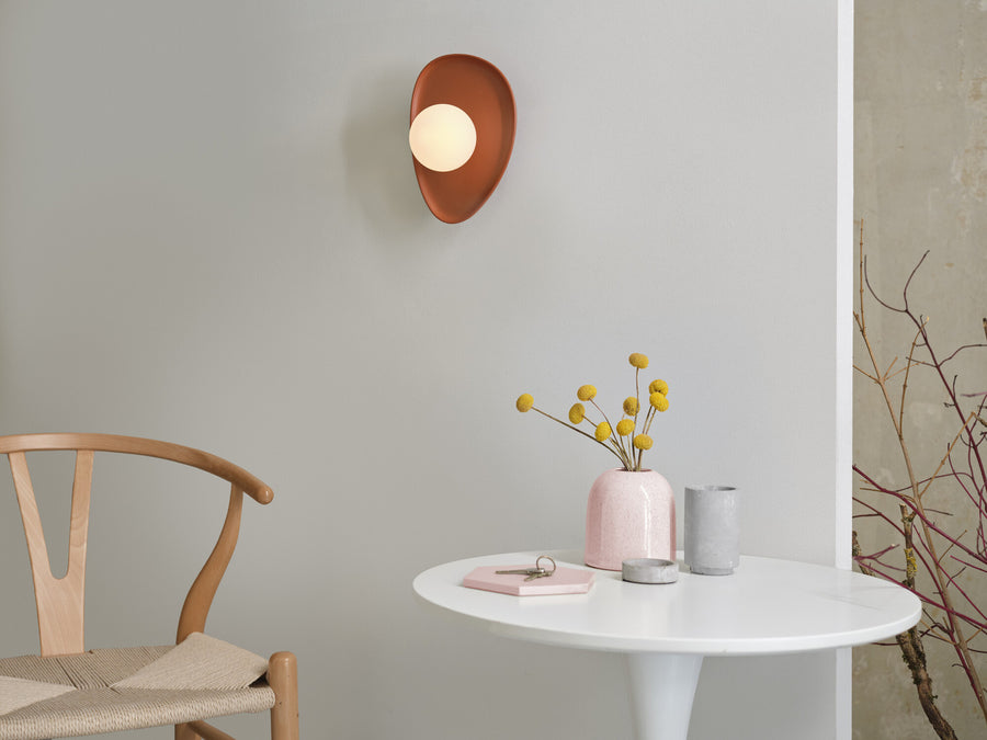 Applique murale brune fixée sur un mur clair au-dessus d’une table avec fleurs jaunes.