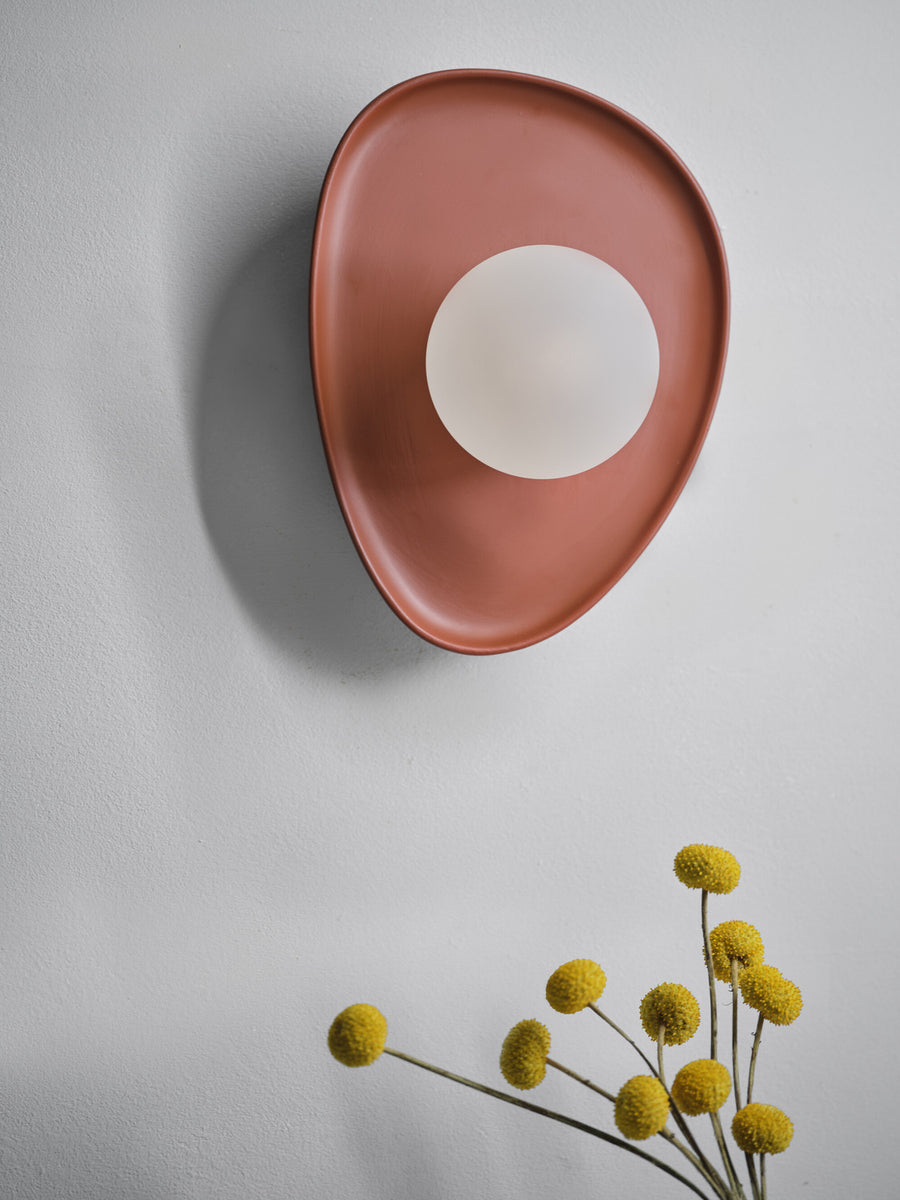 Vue rapprochée de l’applique brune ovale et de son diffuseur blanc sur mur gris.