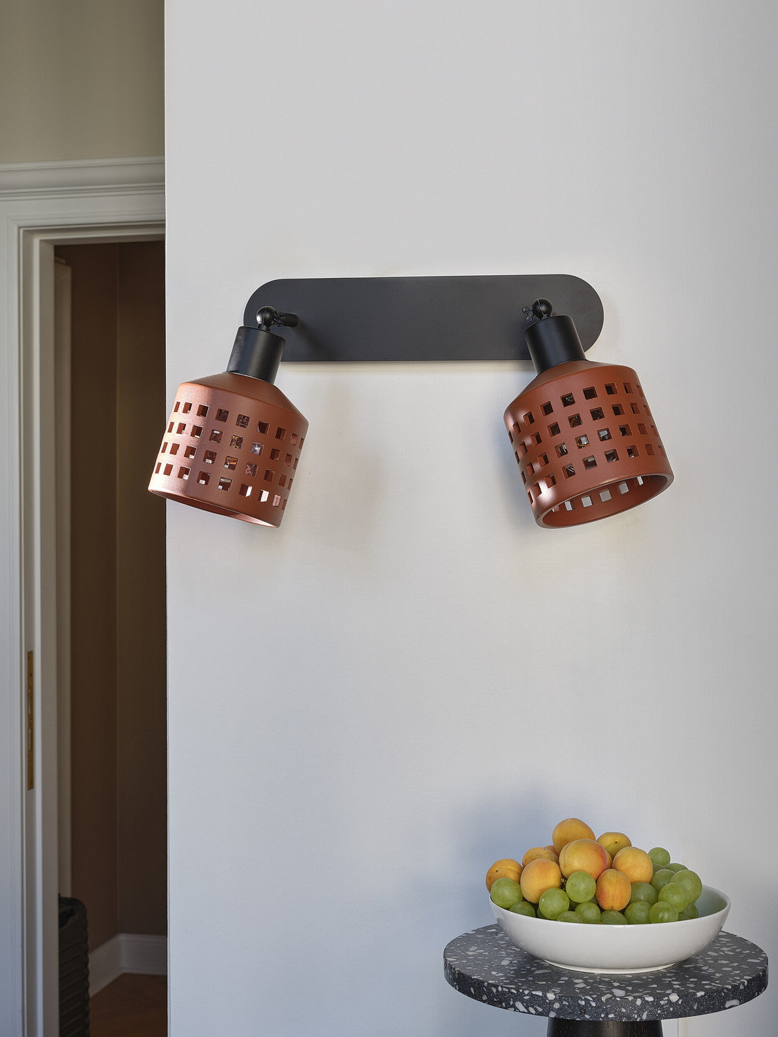 Applique double éteinte sur mur blanc, bol de fruits posé en dessous.