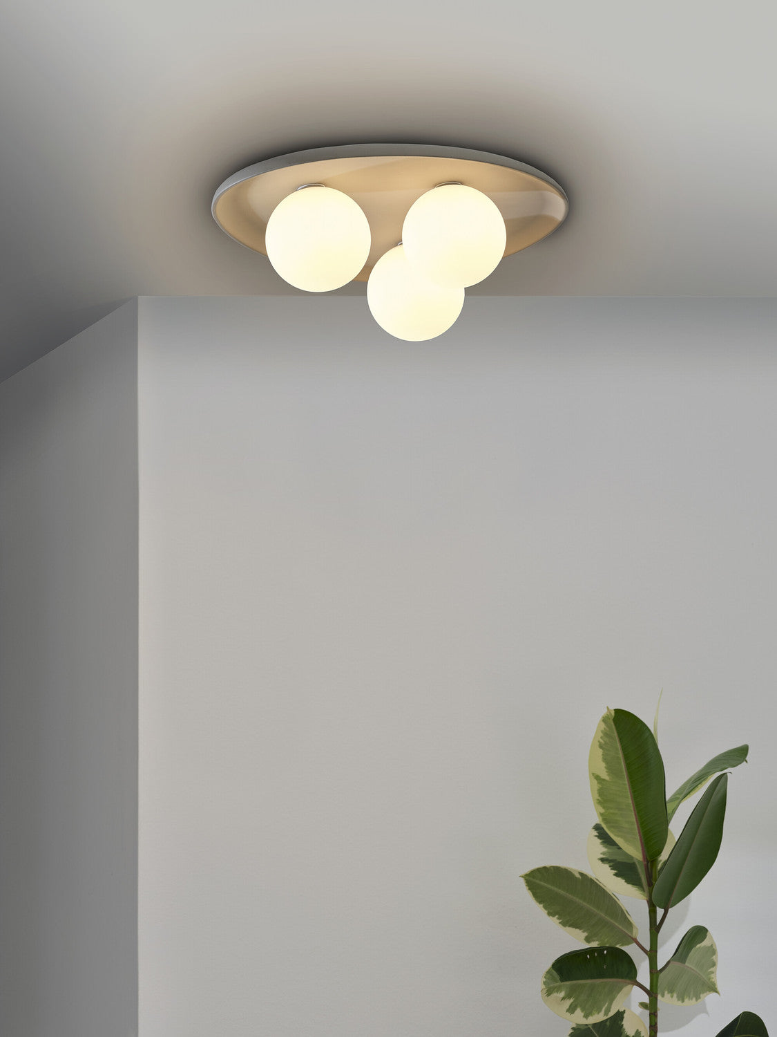 Vue rapprochée du plafonnier allumé, trois globes lumineux sous la plaque grise.