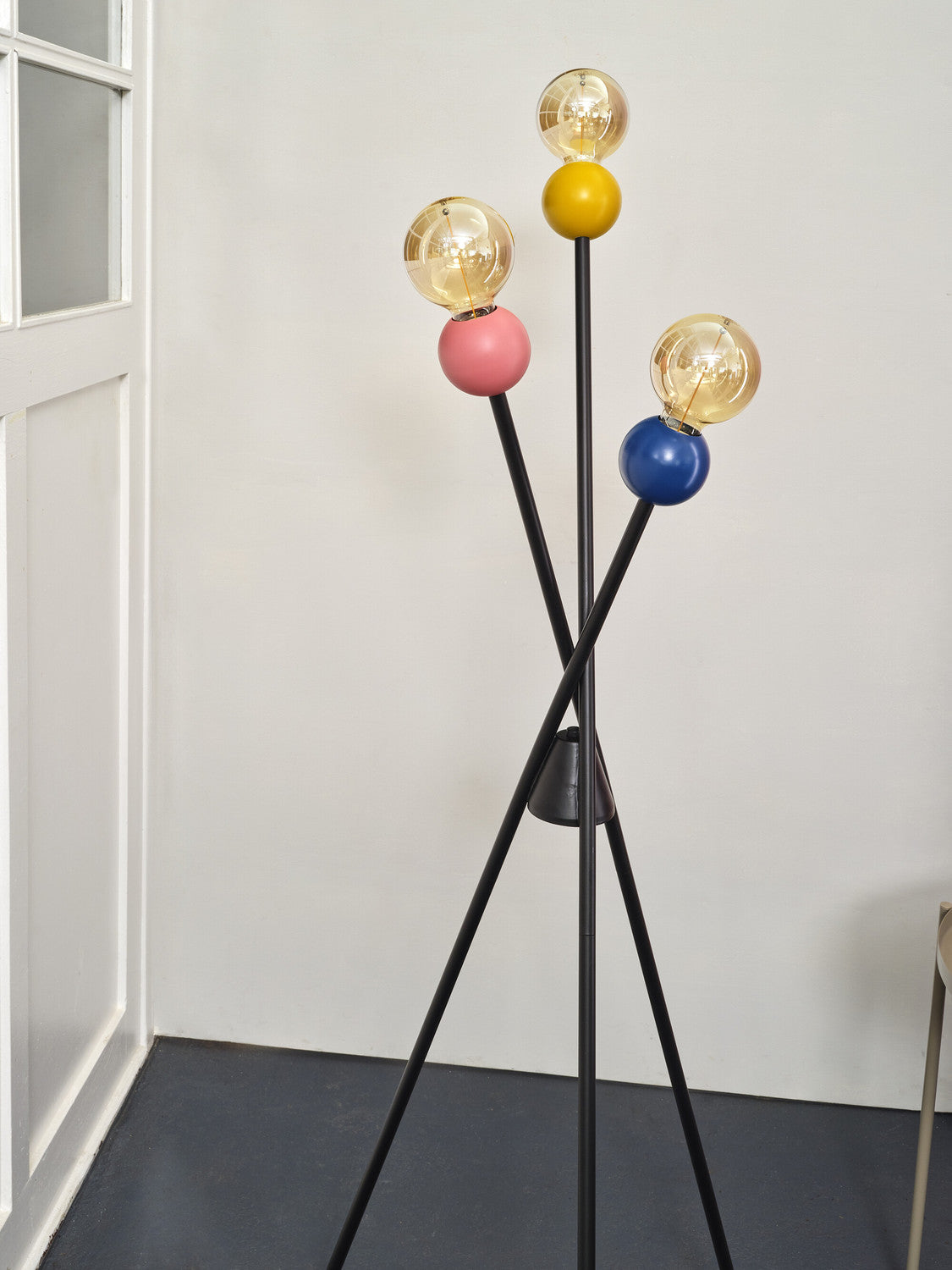 Détail des trois globes colorés et ampoules transparentes allumées sur bras noirs croisés.