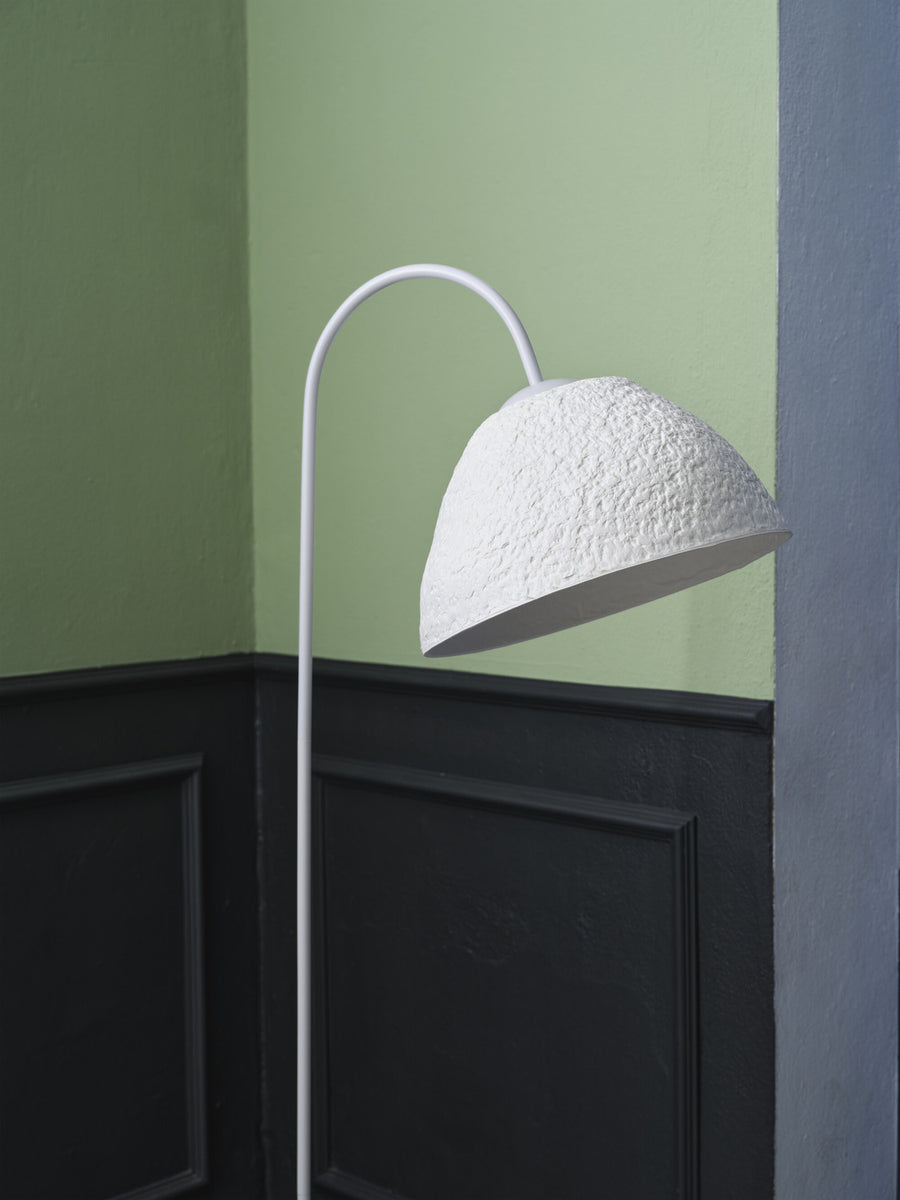 Détail de l'abat-jour blanc texturé et du bras courbé devant un mur vert et noir.