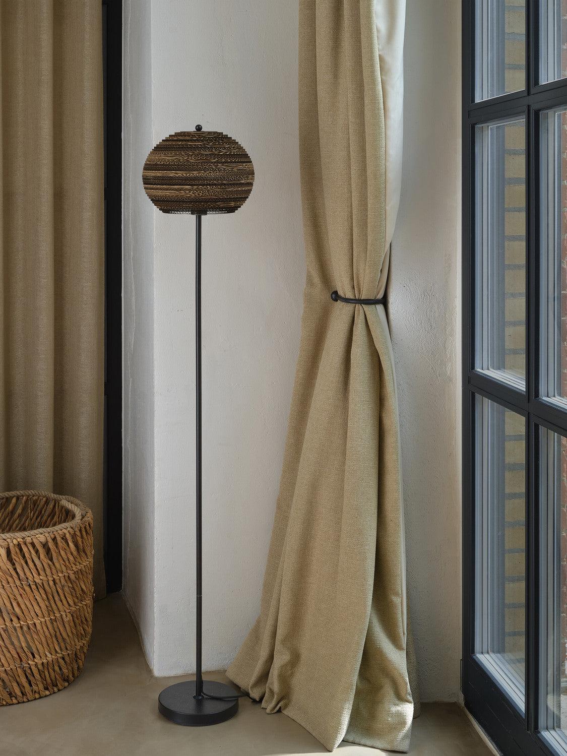 Lampadaire sur pied placé devant une fenêtre, à côté d’un rideau beige et d’un panier.