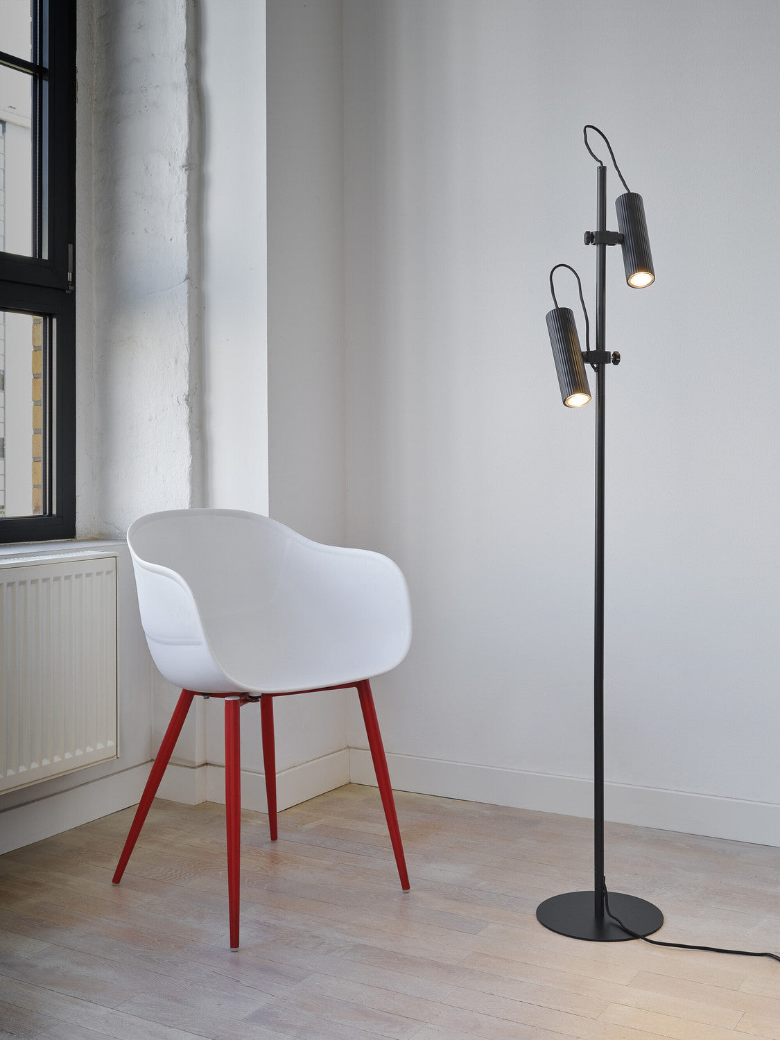Lampadaire noir éclairé placé près d'une chaise blanche aux pieds rouges.
