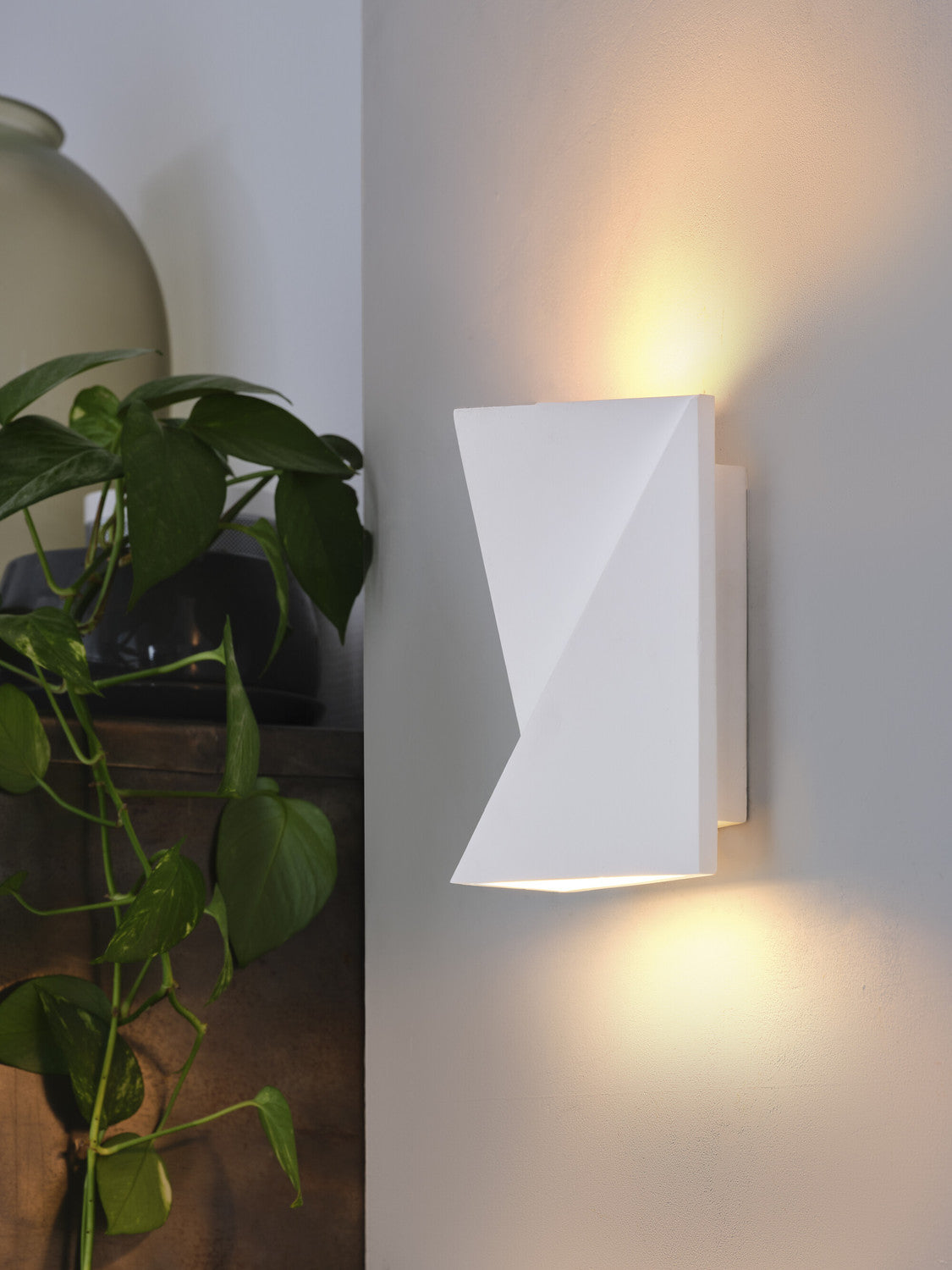 Vue rapprochée de l'applique blanche allumée près d'une plante verte et d'un vase.