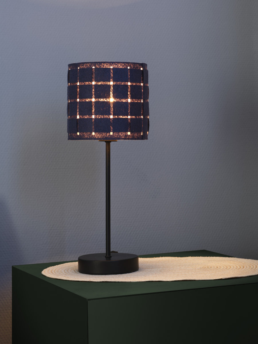 Détail de l'abat-jour allumé, motif tissé et lumière chaude sur fond gris.