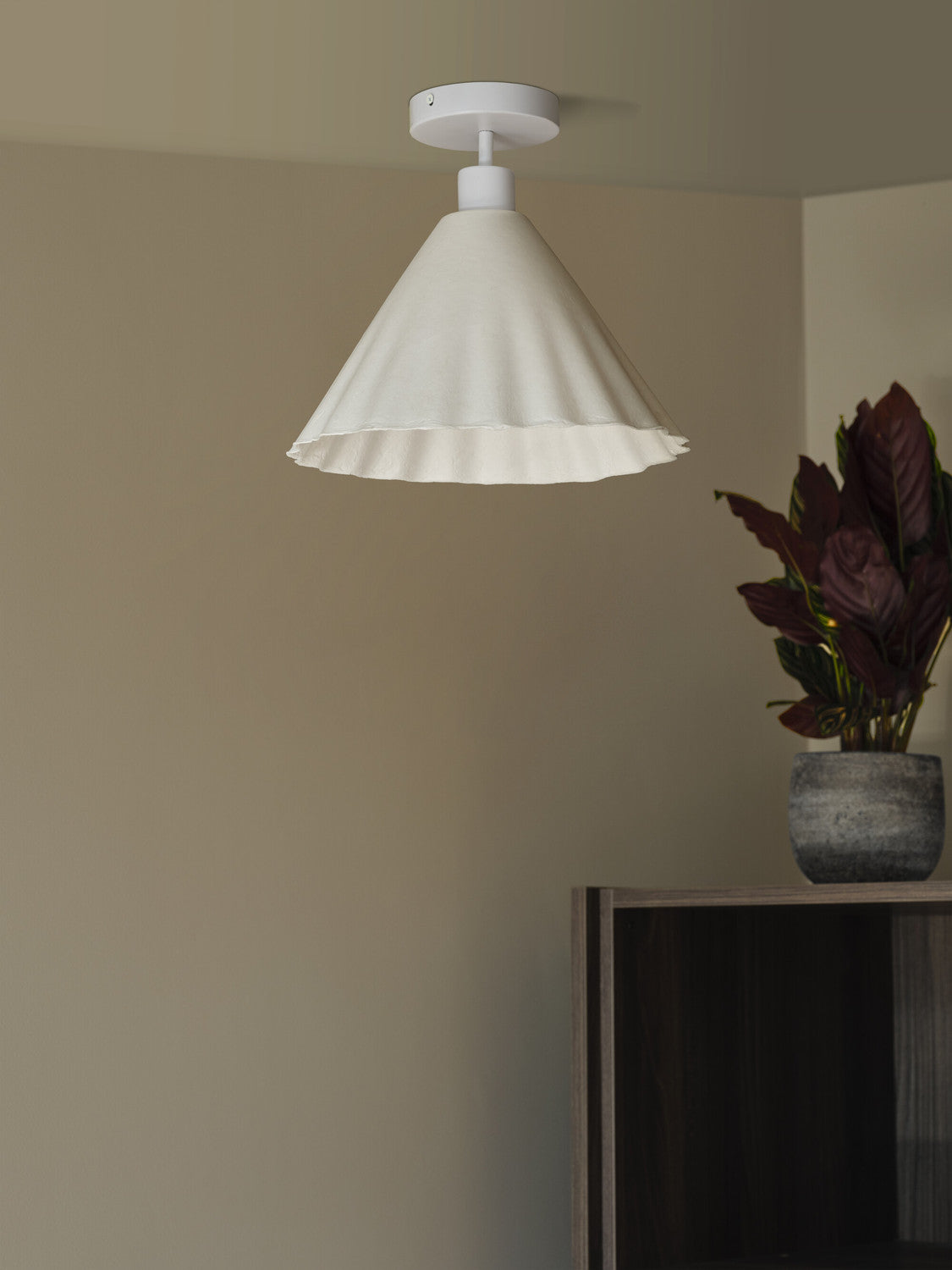 Plafonnier blanc fixé au plafond, allumé au-dessus d'un meuble et d'une plante.