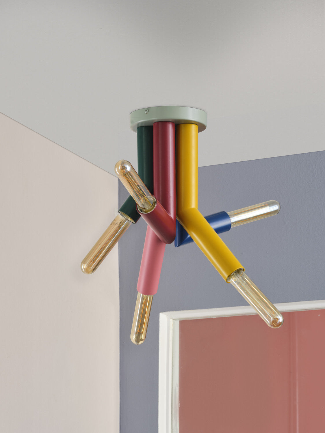 Détail du plafonnier aux bras multicolores équipés d’ampoules à filament, près d’un mur.