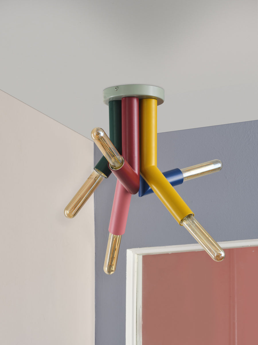 Détail du plafonnier aux bras multicolores équipés d’ampoules à filament, près d’un mur.