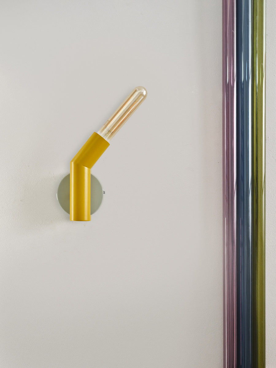 Vue rapprochée de l’applique jaune avec ampoule transparente, près de tubes colorés.