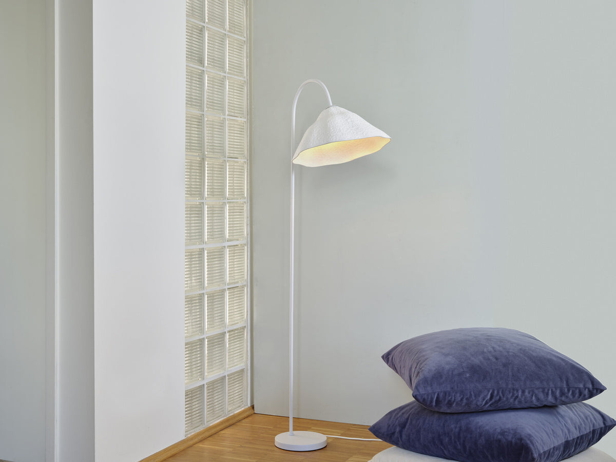 Mise en situation du lampadaire allumé près d'un mur en pavés de verre et coussins.