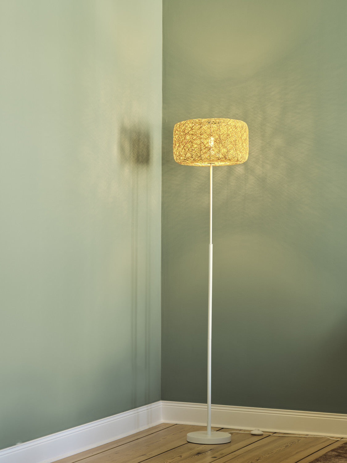 Lampadaire blanc allumé dans un coin de pièce aux murs verts