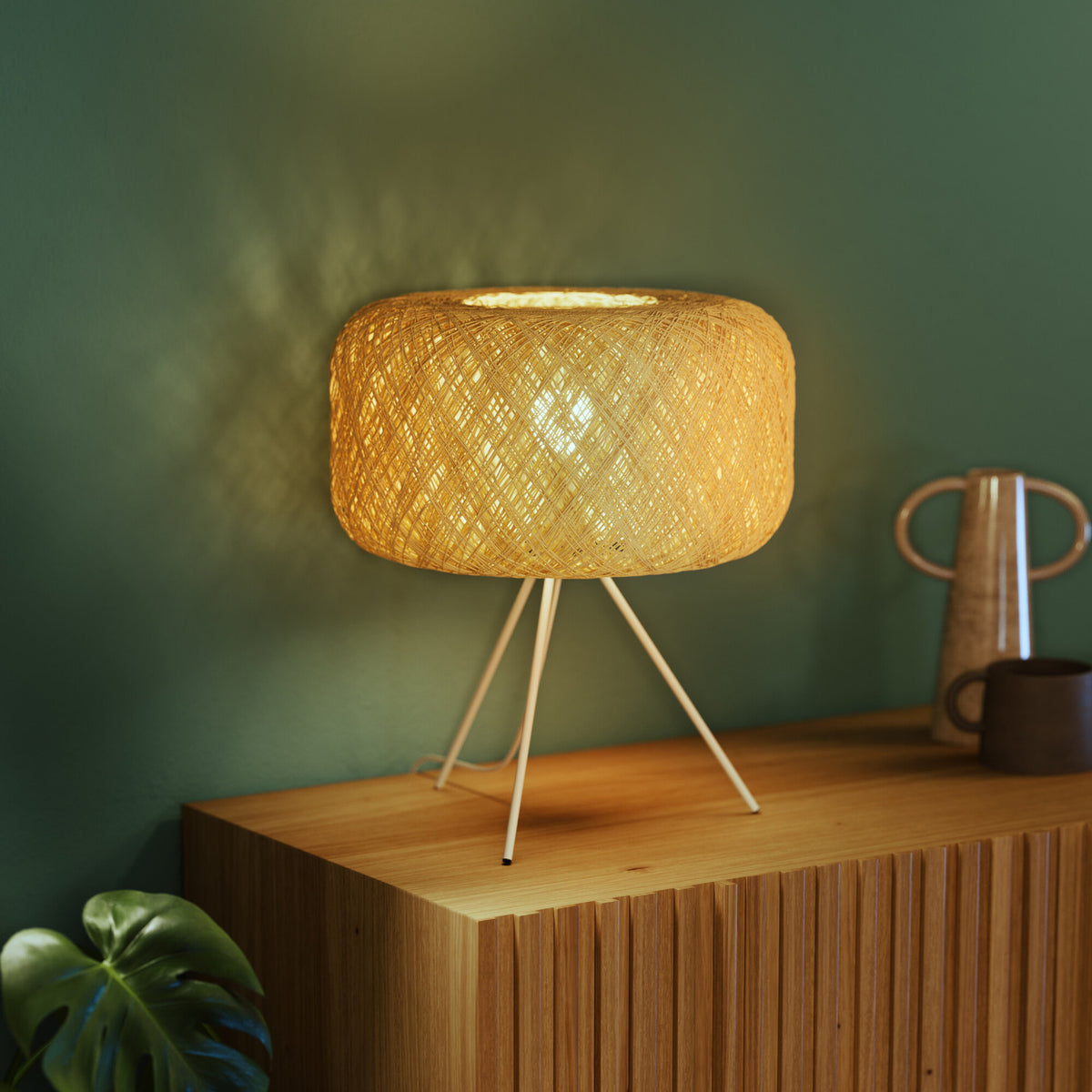 Lampe à poser allumée sur un meuble en bois devant un mur vert.