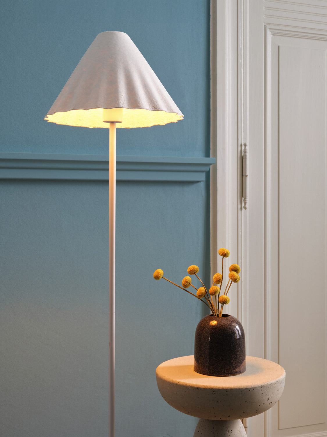 Gros plan sur l'abat-jour conique allumé et un vase à fleurs séchées.
